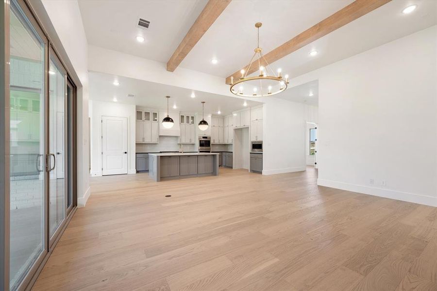 Unfurnished living room with light hardwood / wood-style flooring, an inviting chandelier, and beam ceiling