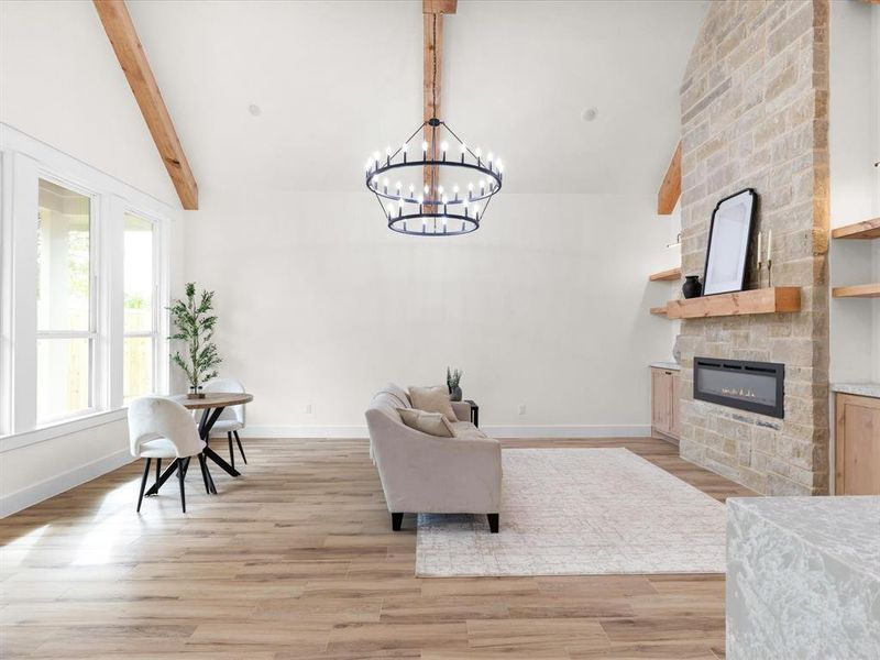 Living room featuring a stone fireplace, light wood-style floors, beam ceiling, a chandelier, and high vaulted ceiling