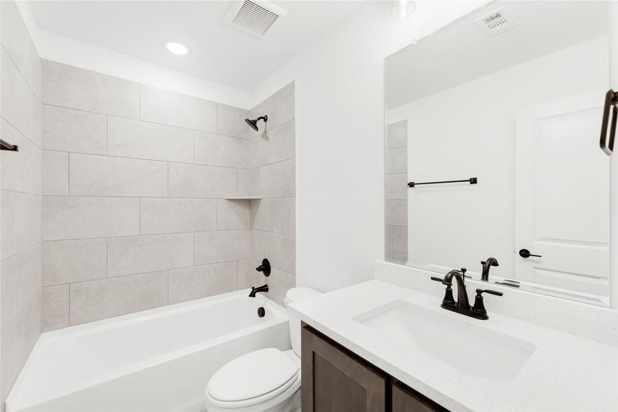Bathroom with tiled tub-shower combo, white quartz vanity, dark hardware, and toilet Bathroom with tiled tub-shower combo, white quartz vanity, dark hardware, and toilet