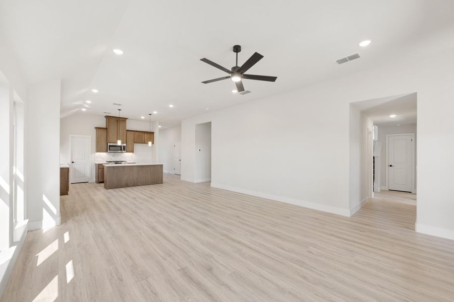 Open-concept living area with light wood floors, ceiling fan, and kitchen with island visible in background