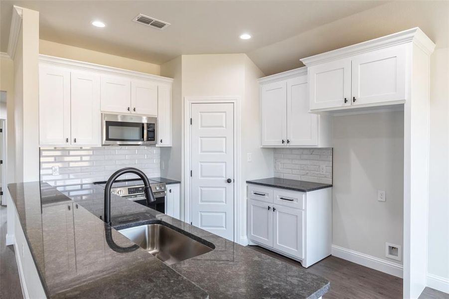 Modern kitchen featuring a large island with an undermount sink and matte black faucet, stainless steel microwave, white shaker-style cabinetry, and subway tile backsplash