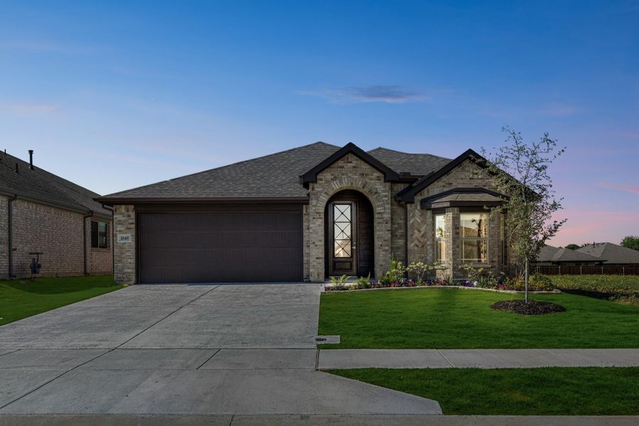 Single-story brick home with arched entryway, two-car garage, and landscaped front yard at dusk.