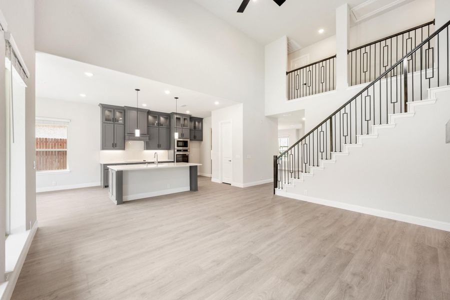 Open-concept living area with kitchen island, gray cabinets, high ceilings, and staircase with iron balusters