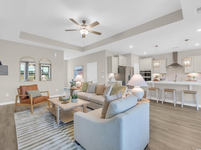 Living area with a raised ceiling, light wood-type flooring, ceiling fan, recessed lighting, and a chandelier