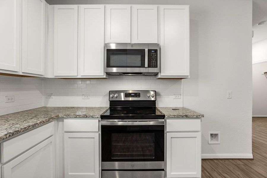 Kitchen with stainless steel appliances, light stone counters, decorative backsplash, and white cabinetry