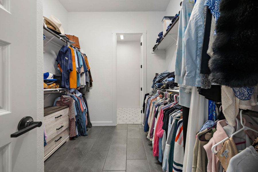 Walk-in closet featuring dark tile flooring, built-in shelving, and hanging rods