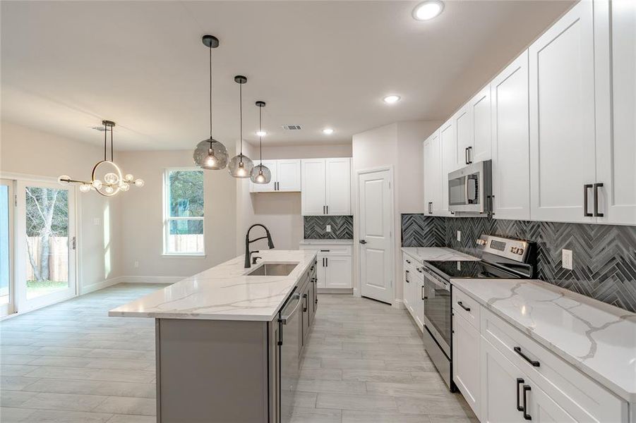 Kitchen featuring a kitchen island with sink, sink, appliances with stainless steel finishes, decorative light fixtures, and white cabinetry