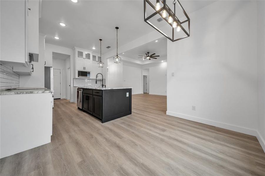 Kitchen featuring decorative backsplash, appliances with stainless steel finishes, light wood-type flooring, decorative light fixtures, and white cabinets