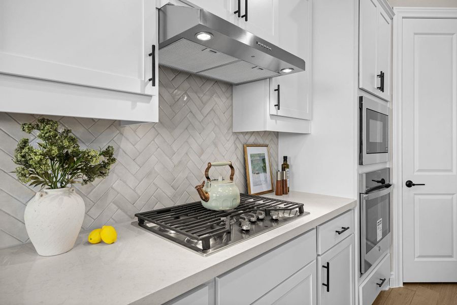 Kitchen with under cabinet range hood, white cabinets, backsplash, and stainless steel appliances