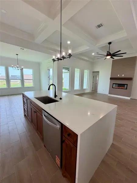 Spacious kitchen island featuring a waterfall-edge countertop, undermount sink, and integrated dishwasher
