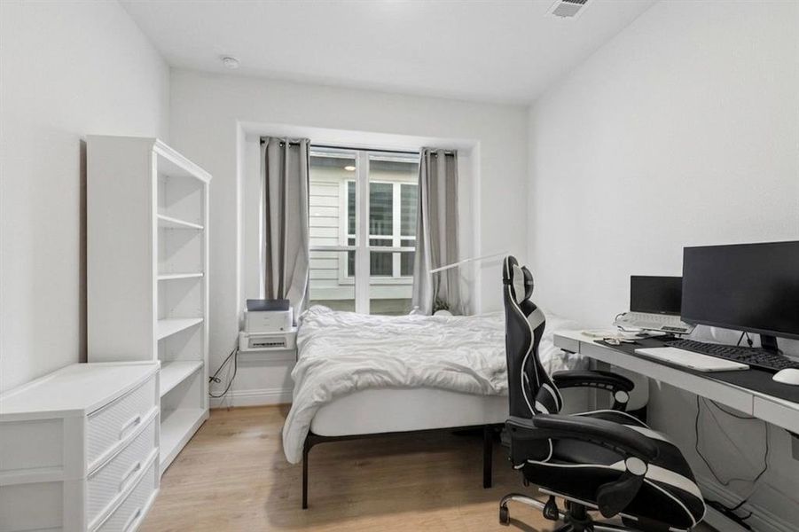 Bright interior space featuring a window with gray drapes, wood-finish flooring, and white painted walls