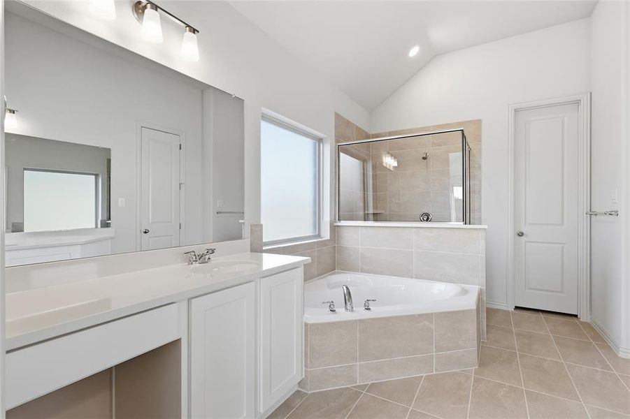 Full bathroom featuring vaulted ceiling, a garden tub, light tile patterned flooring, vanity, and a stall shower