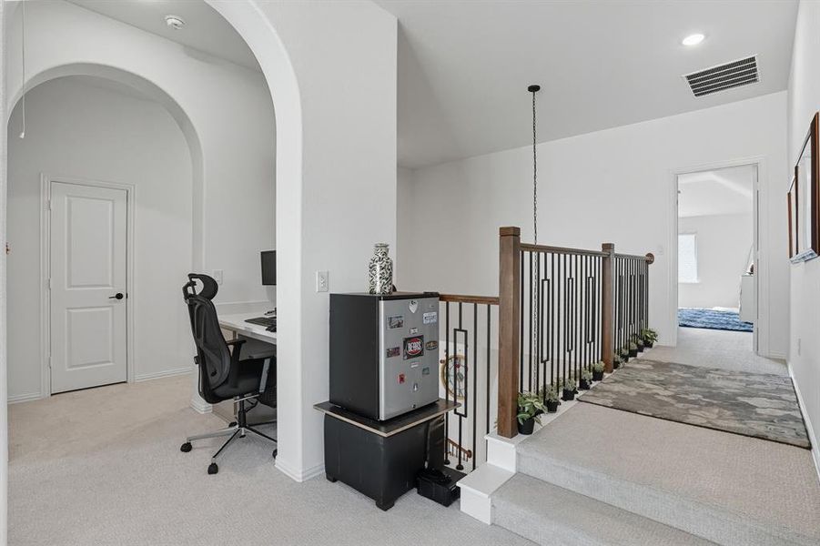Upper-level landing featuring a wood and wrought iron staircase railing, light gray carpet, and an arched doorway leading to an additional room