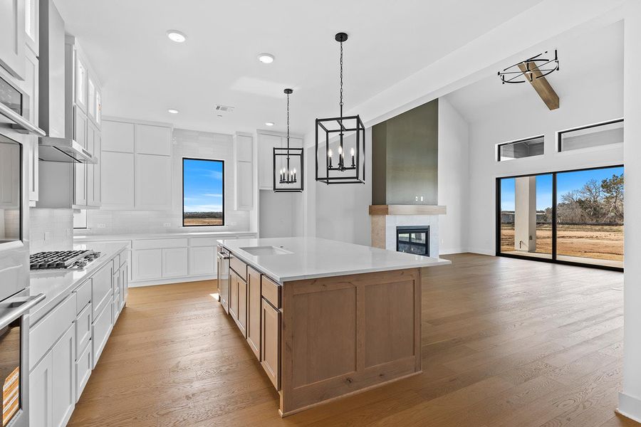 Kitchen featuring a center island, light wood-style floors, a tile fireplace, dual tone cabinets, and decorative backsplash