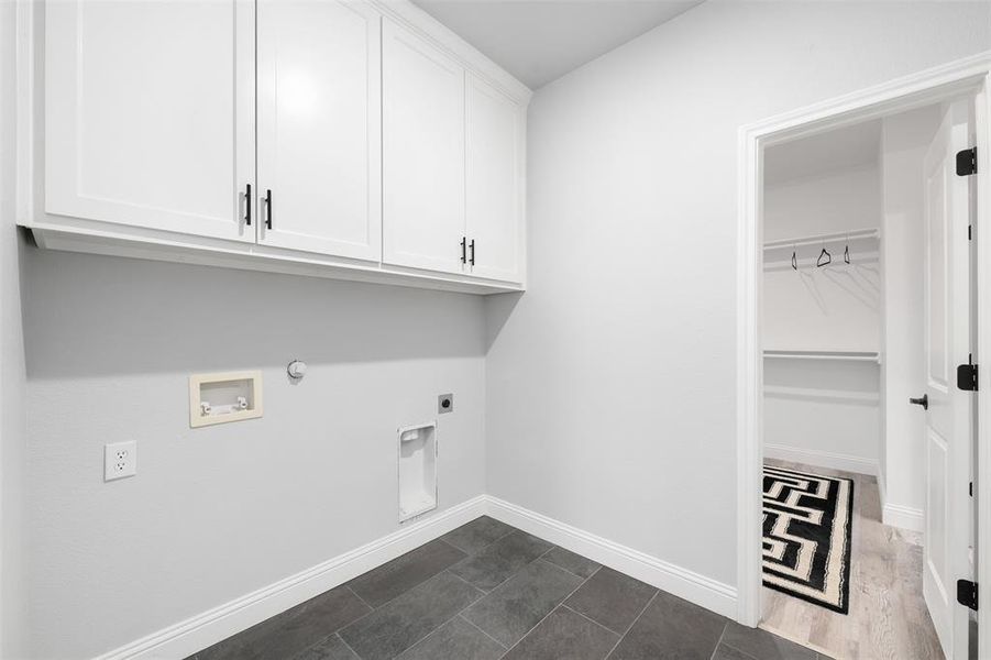 Washroom with gas dryer hookup, electric dryer hookup, cabinets, washer hookup, and dark tile patterned flooring