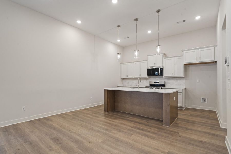 Spacious living area featuring wood-finish flooring, recessed lighting, and a modern kitchen Spacious living area featuring wood-finish flooring, recessed lighting, and a modern kitchen