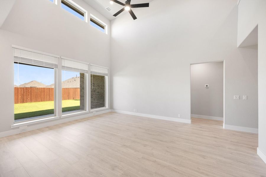 Empty living room with high ceilings, ceiling fan, light wood floors, and large windows overlooking backyard Empty living room with high ceilings, ceiling fan, light wood floors, and large windows overlooking backyard