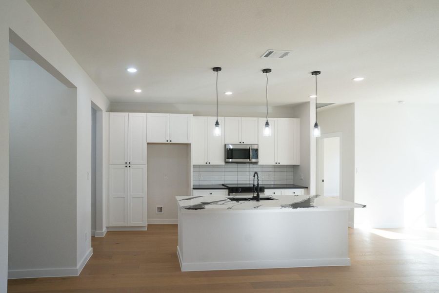 Kitchen with white cabinetry, pendant lighting, decorative backsplash, stainless steel microwave, and a center island with sink