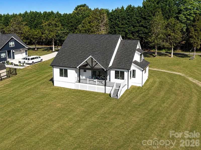 Expansive aerial view showcasing the beautifully designed modern farmhouse, spacious backyard, and peaceful setting surrounded by mature trees for added privacy. (Concept grass)