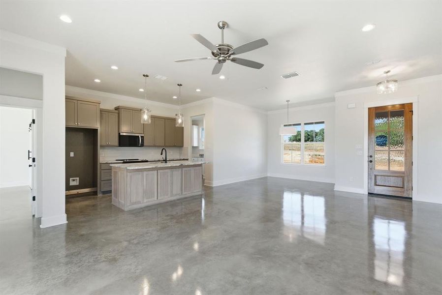 Kitchen with open floor plan, decorative light fixtures, concrete floors, ornamental molding, and a center island with sink