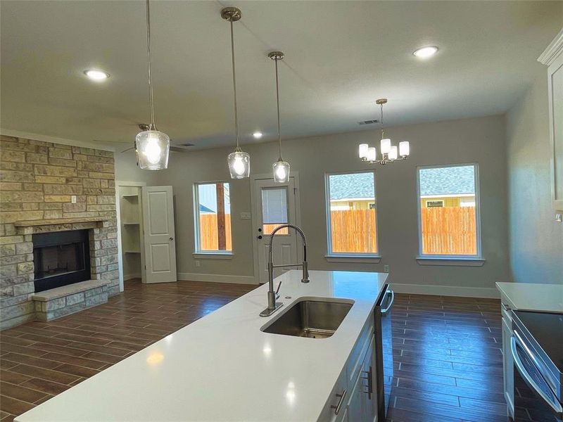 Kitchen featuring range with electric cooktop, a stone fireplace, pendant lighting, sink, and a notable chandelier