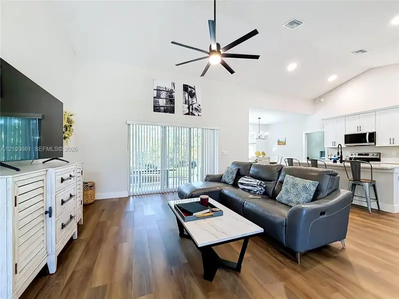 Living area featuring vaulted ceilings, wood-finish flooring, multi-blade ceiling fan, and sliding glass doors