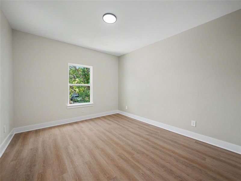 Room featuring wood-finish flooring, neutral wall tones, a single window, and a flush-mount ceiling light Room featuring wood-finish flooring, neutral wall tones, a single window, and a flush-mount ceiling light