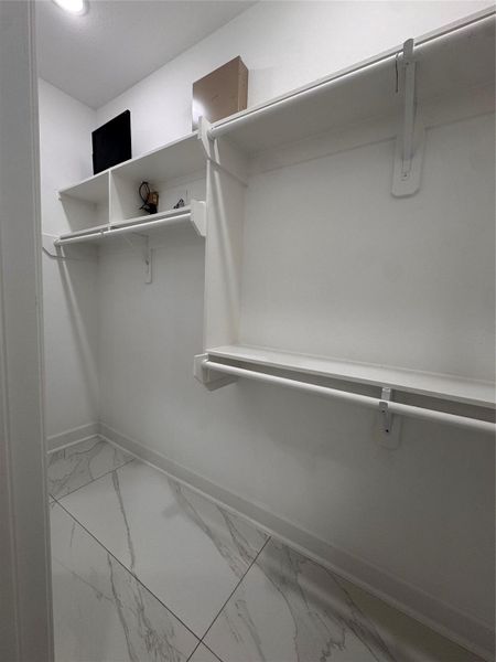Spacious walk-in closet featuring sleek white shelving and elegant marble-like tile flooring, perfect for organizing your wardrobe. Spacious walk-in closet featuring sleek white shelving and elegant marble-like tile flooring, perfect for organizing your wardrobe.