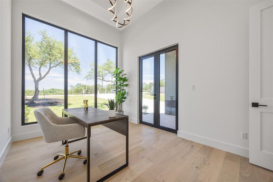 A well-lit study or bedroom #2 with generous windows overlooking the tranquil outdoors, featuring light-toned hardwood flooring.