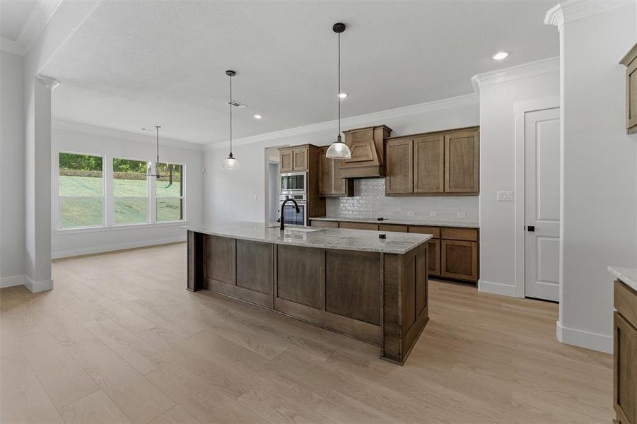Open-concept kitchen featuring a central island with a stone countertop, wood-finish cabinetry, built-in appliances, and light wood-finish flooring