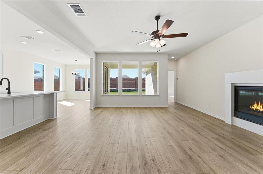 Unfurnished living room with a glass covered fireplace, a chandelier, recessed lighting, light wood-type flooring, and a ceiling fan