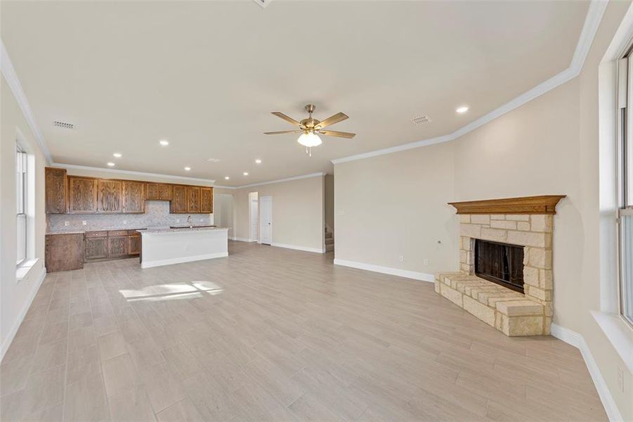 Unfurnished living room with a stone fireplace, ceiling fan, and ornamental molding