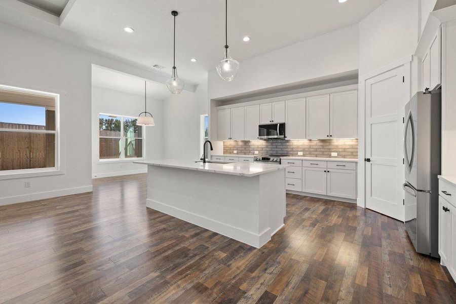Kitchen with stainless steel appliances, a center island with sink, decorative backsplash, and white cabinetry