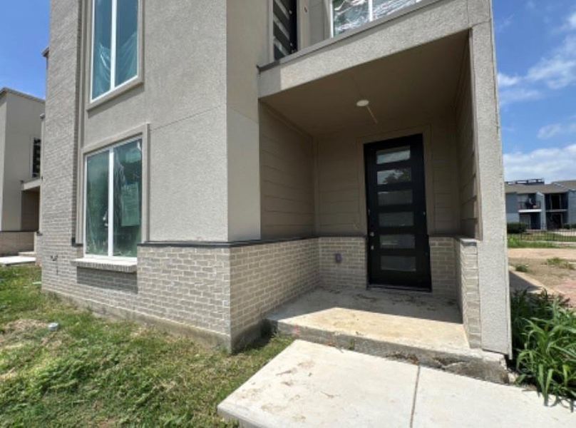Property entrance featuring brick siding, a balcony, and stucco siding Property entrance featuring brick siding, a balcony, and stucco siding