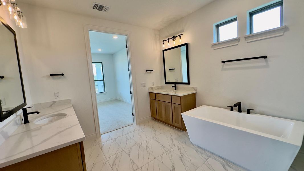 Full bath with two vanities, light marble finish flooring, a soaking tub, and recessed lighting