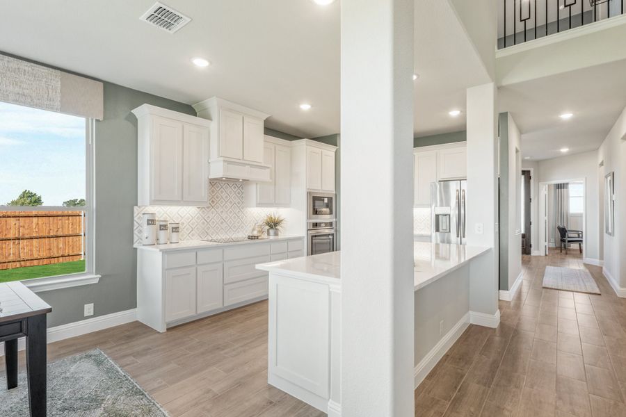 Kitchen with white cabinets, patterned tile backsplash, stainless steel appliances, and center island on wood-look floors
