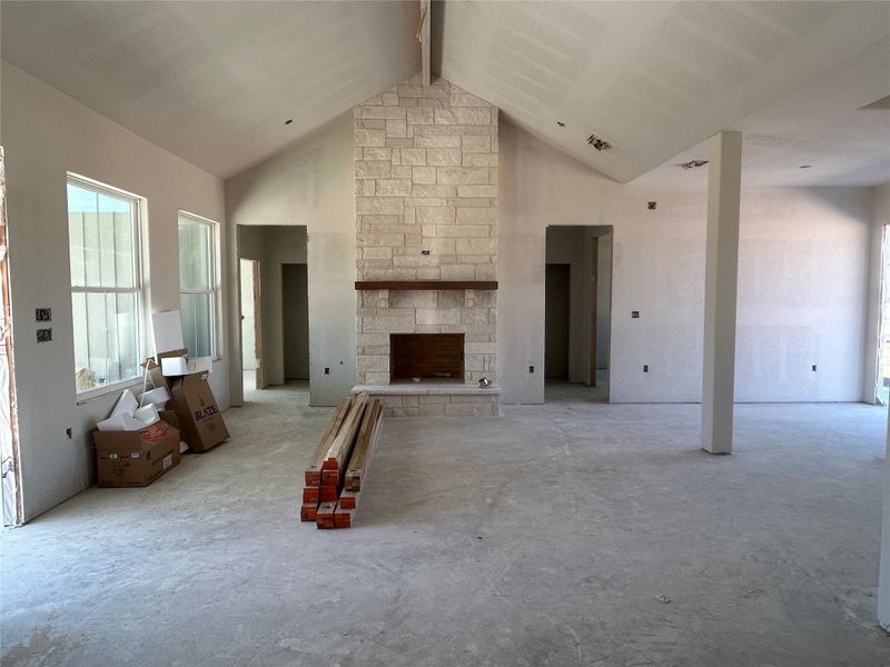 Unfurnished living room with healthy amount of natural light, a stone fireplace, and concrete flooring