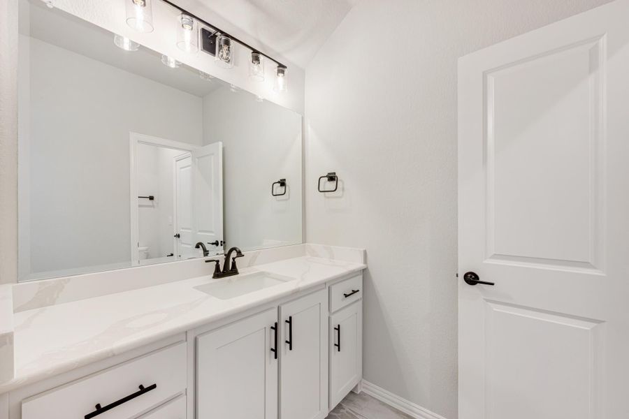 Bathroom with white vanity, quartz countertop, large mirror, and black hardware accents Bathroom with white vanity, quartz countertop, large mirror, and black hardware accents