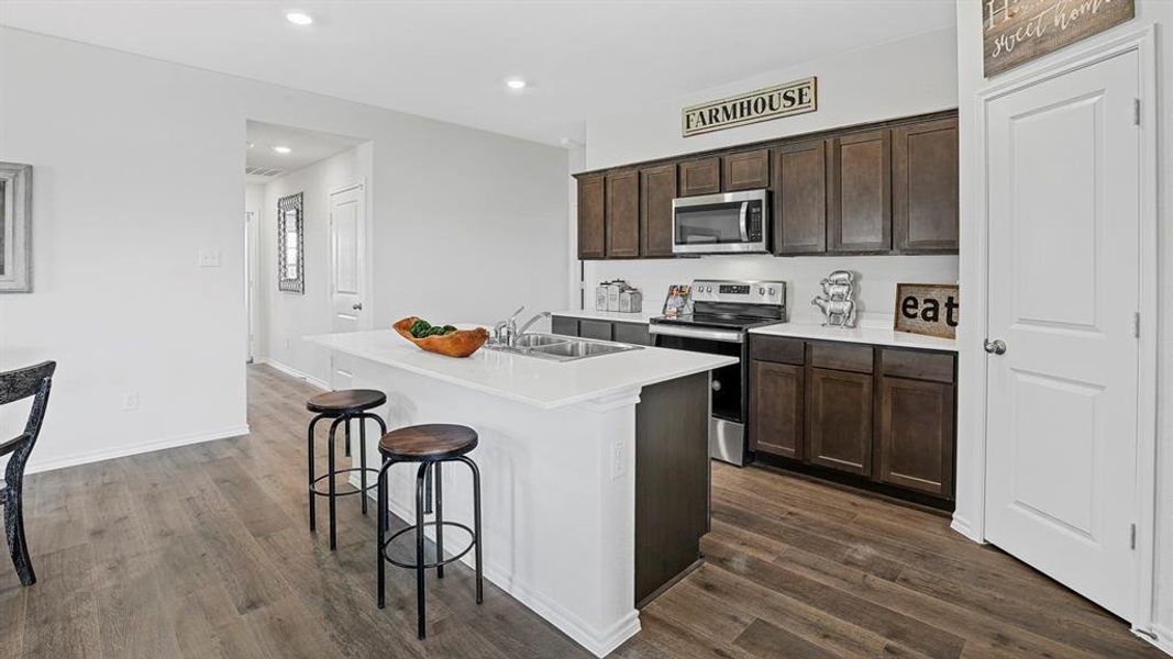 Modern kitchen featuring wood-finish flooring, white countertops, dark wood cabinetry, stainless steel appliances, and a central island with integrated sink