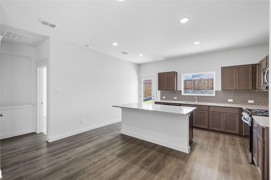 Kitchen with decorative backsplash, appliances with stainless steel finishes, light stone countertops, a center island, and recessed lighting Kitchen with decorative backsplash, appliances with stainless steel finishes, light stone countertops, a center island, and recessed lighting