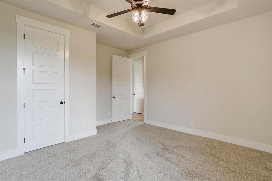 Unfurnished bedroom featuring light carpet, a tray ceiling, and ceiling fan