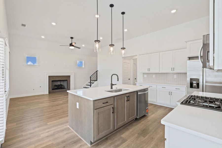Kitchen island with a stainless steel sink, stainless steel appliances, wood-finish flooring, white cabinetry, and a fireplace Kitchen island with a stainless steel sink, stainless steel appliances, wood-finish flooring, white cabinetry, and a fireplace