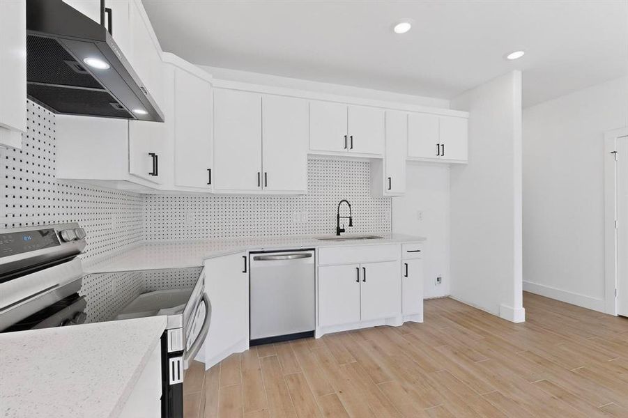 Kitchen featuring under cabinet range hood, appliances with stainless steel finishes, white cabinets, light wood-style flooring, and light stone countertops