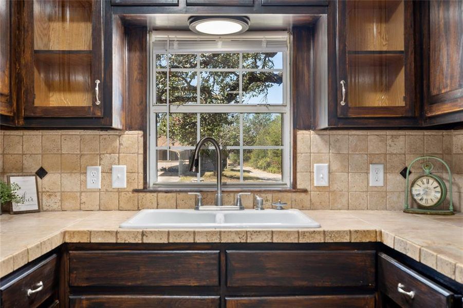 Kitchen featuring dark brown cabinets, decorative backsplash, and tile countertops