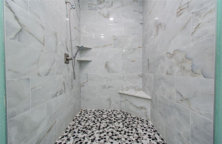 This bathroom features a spacious walk-in shower with elegant marble-patterned tiles and a stylish mosaic floor. It includes built-in shelves for storage and modern fixtures for a luxurious feel.