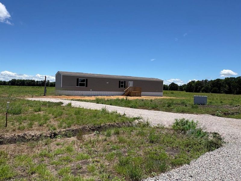 Manufactured home featuring neutral-toned siding, dark window shutters, and a light-colored foundation Manufactured home featuring neutral-toned siding, dark window shutters, and a light-colored foundation