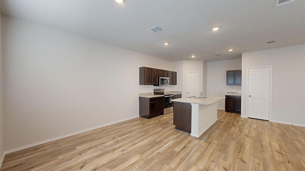 Kitchen featuring stainless steel appliances, a kitchen island with sink, dark wood finish cabinetry, light wood finished floors, and recessed lighting