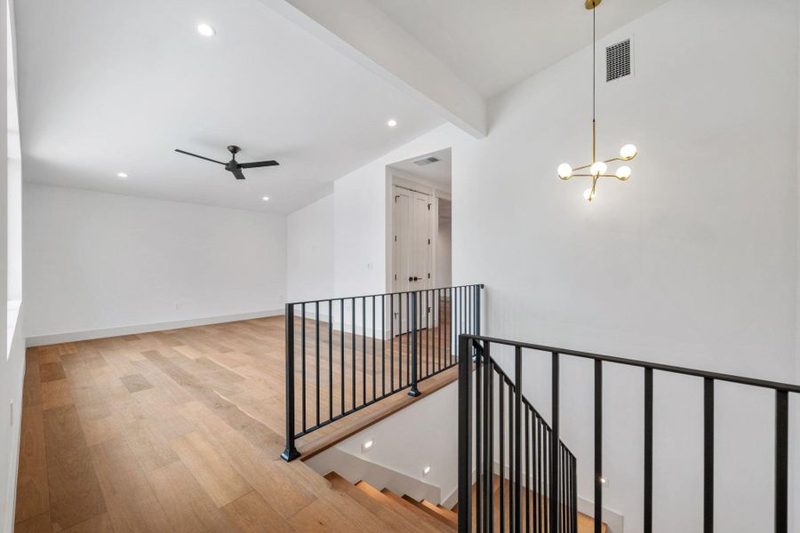 Hallway with light wood-style flooring, suspended lighting, an upstairs landing, and vaulted ceiling