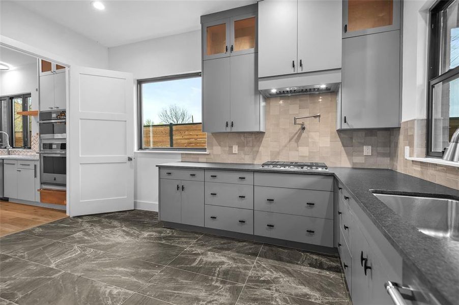 Kitchen with dark stone countertops, gray cabinets, stainless steel appliances, and decorative backsplash