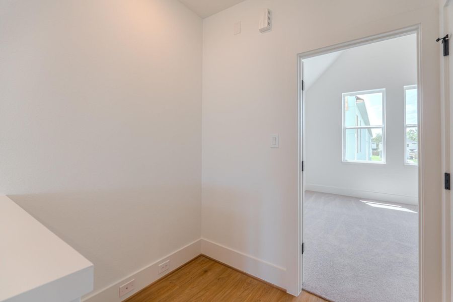 This photo shows a bright, open room with light-colored walls and wood flooring. The adjacent room has large windows allowing natural light to fill the space, highlighting its neutral carpet and high ceilings.Photo Disclaimer: Photos are representative of the community and may depict a similar floor plan, model home, or previously completed residence. This photo shows a bright, open room with light-colored walls and wood flooring. The adjacent room has large windows allowing natural light to fill the space, highlighting its neutral carpet and high ceilings.Photo Disclaimer: Photos are representative of the community and may depict a similar floor plan, model home, or previously completed residence.